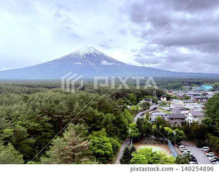 Mount Fuji rises in the distance beyond the townscape of Yamanashi Prefecture and the lush green forest. Mount Fuji rises in the distance beyond the townscape of Yamanashi Prefecture and the lush green forest. 140254896