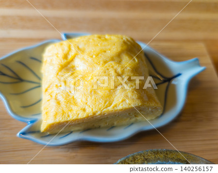 A leaf-shaped dish and a fluffy rolled omelet, placed on a wooden tray. A leaf-shaped dish and a fluffy rolled omelet, placed on a wooden tray. 140256157