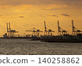 Industrial port cranes silhouetted against a dramatic golden sunset sky over the water 140258862