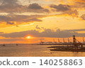 Golden sunset over a busy industrial port with cargo ships and cranes 140258863