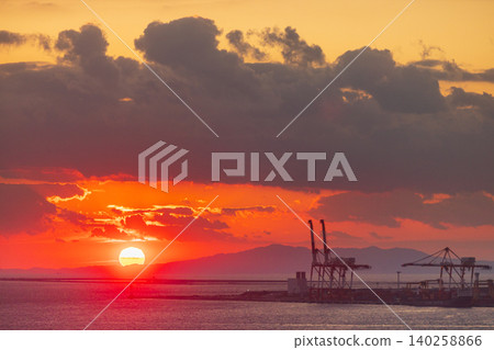 Vibrant sunset over the ocean with industrial cranes and distant mountains 140258866