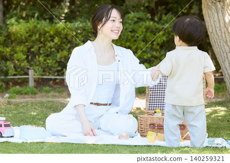 A mother and young child enjoying a picnic on the park's lawn. 140259321