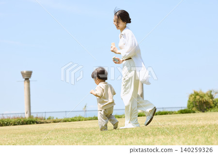 在陽光明媚的日子裡,一位母親帶著她的小兒子在綠草茵茵的公園散步。 在陽光明媚的日子裡,一位母親帶著她的小兒子在綠草茵茵的公園散步。 140259326