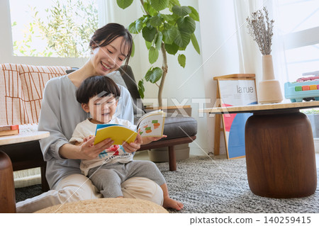 A smiling toddler sitting on his mother's lap in the living room, reading a picture book. A smiling toddler sitting on his mother's lap in the living room, reading a picture book. 140259415
