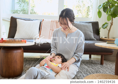 A smiling mother brushes her child's teeth in the living room. A smiling mother brushes her child's teeth in the living room. 140259416