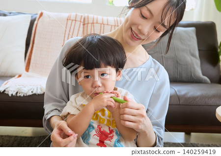 A young mother smiles as she brushes her child's teeth in the living room. A young mother smiles as she brushes her child's teeth in the living room. 140259419