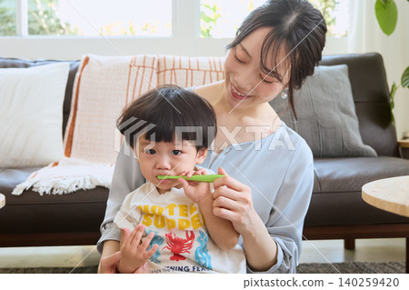 A young mother smiles as she brushes her child's teeth in the living room. A young mother smiles as she brushes her child's teeth in the living room. 140259420