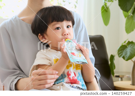 A toddler eating organic baby food on his mother's lap. A toddler eating organic baby food on his mother's lap. 140259427