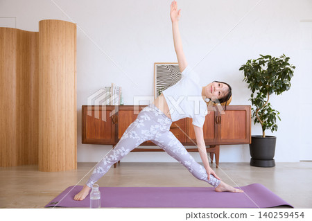 A young woman doing the triangle pose in her living room at home. A young woman doing the triangle pose in her living room at home. 140259454