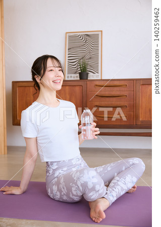 A smiling young woman rehydrating on a yoga mat. A smiling young woman rehydrating on a yoga mat. 140259462