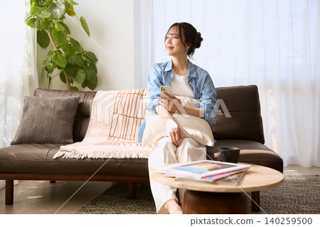 A young woman relaxing on the living room sofa with her smartphone in hand. A young woman relaxing on the living room sofa with her smartphone in hand. 140259500