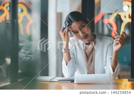 Exhausted businesswoman holding glasses and pen at office desk, feeling stressed by paperwork, mistakes and deadlines while pausing during a demanding professional workday at the workplace. Exhausted businesswoman holding glasses and pen at office desk, feeling stressed by paperwork, mistakes and deadlines while pausing during a demanding professional workday at the workplace. 140259854