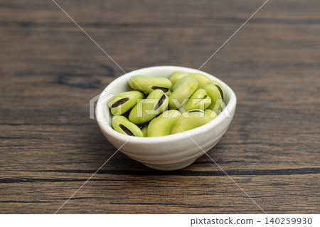 Raw broad beans in a small white bowl; wood-grain background and copy space. Raw broad beans in a small white bowl; wood-grain background and copy space. 140259930