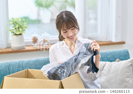 A smiling woman takes clothes out of a cardboard box. A smiling woman takes clothes out of a cardboard box. 140260115