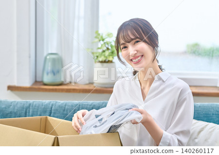 一位女士欣喜地打開了快遞送來的衣物包裹。 一位女士欣喜地打開了快遞送來的衣物包裹。 140260117