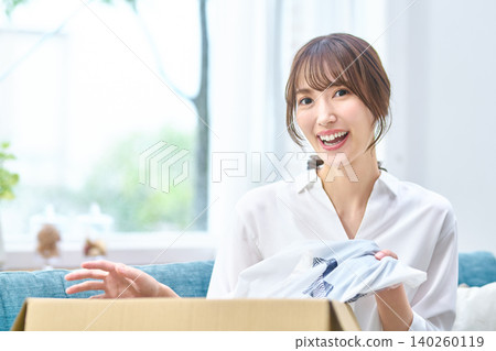 A woman with a happy smile takes out clothes that arrived in a cardboard box. A woman with a happy smile takes out clothes that arrived in a cardboard box. 140260119
