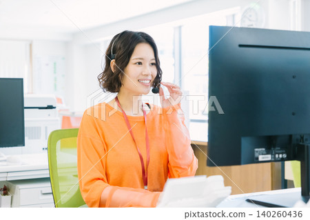 辦公室裡,一名戴著耳機的女接線生正在接聽電話。 辦公室裡,一名戴著耳機的女接線生正在接聽電話。 140260436
