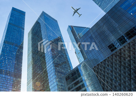 Modern glass skyscrapers on a clear day and passenger plane flying over Modern glass skyscrapers on a clear day and passenger plane flying over 140260620
