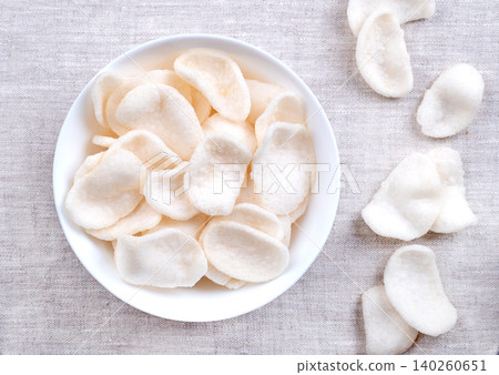 Prawn crackers, shrimp chips in a white bowl on linen. Deep-fried crackers made from a dough of tapioka, ground prawns, and seasonings. A popular snack and side dish in Southeast Asian cuisine. Photo Prawn crackers, shrimp chips in a white bowl on linen. Deep-fried crackers made from a dough of tapioka, ground prawns, and seasonings. A popular snack and side dish in Southeast Asian cuisine. Photo 140260651