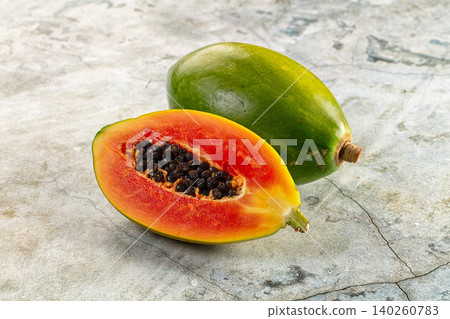 Fresh papaya fruit whole and halved showing orange flesh and black seeds on stone surface Fresh papaya fruit whole and halved showing orange flesh and black seeds on stone surface 140260783