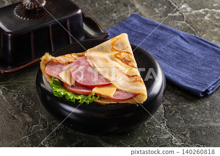 Savory folded crepe with ham cheese and lettuce on dark plate Savory folded crepe with ham cheese and lettuce on dark plate 140260818