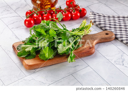Fresh green cilantro bunch on wooden cutting board with cherry tomatoes and oil bottle Fresh green cilantro bunch on wooden cutting board with cherry tomatoes and oil bottle 140260846