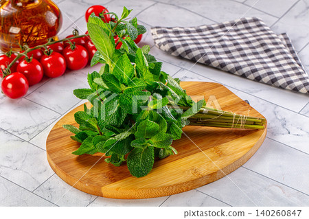 Fresh mint bunch on wooden cutting board with tomatoes and oil Fresh mint bunch on wooden cutting board with tomatoes and oil 140260847
