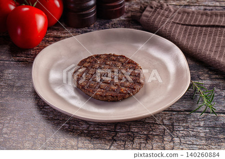 Grilled beef patty on ceramic plate with fresh tomatoes and rosemary 140260884