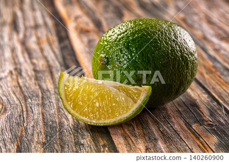 fresh green lime and sliced wedge on rustic wooden table fresh green lime and sliced wedge on rustic wooden table 140260900