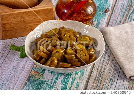 Sliced pickled jalapeno peppers in a white bowl on a rustic wooden table Sliced pickled jalapeno peppers in a white bowl on a rustic wooden table 140260943