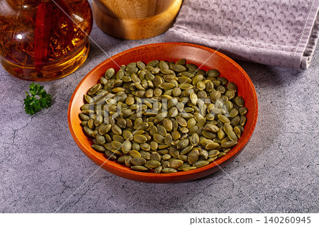 Hulled green pumpkin seeds in a rustic wooden bowl on a grey textured background 140260945