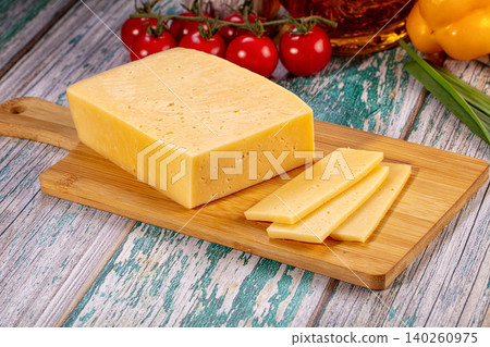 yellow cheese block and slices on wooden cutting board with tomatoes and vegetables 140260975