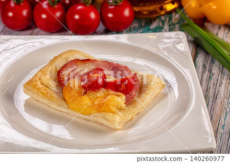 Puff pastry tart with sausage, cheese, and tomatoes on white plate 140260977