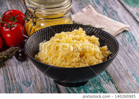 Couscous in black bowl with tomatoes and jar on rustic wooden table 140260985