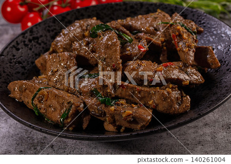 Spicy fried beef liver with basil and chili pepper in black bowl, close-up Spicy fried beef liver with basil and chili pepper in black bowl, close-up 140261004