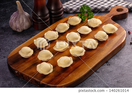Raw dumplings on wooden board with garlic and pepper mills Raw dumplings on wooden board with garlic and pepper mills 140261014