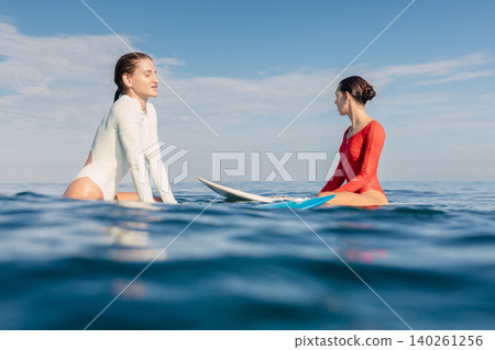 Two girl surfers sitting on surfboards in calm ocean waiting for surfing waves Two girl surfers sitting on surfboards in calm ocean waiting for surfing waves 140261256