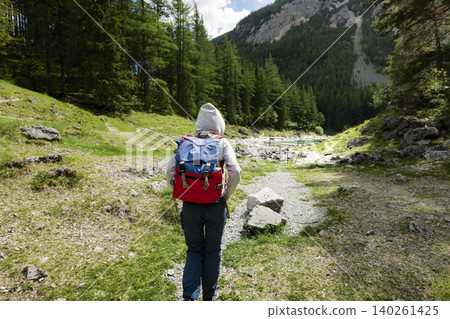 Traveler wearing a hoodie and backpack walks along a trail in the Austrian Alps, highlighting exploring mountain landscapes Traveler wearing a hoodie and backpack walks along a trail in the Austrian Alps, highlighting exploring mountain landscapes 140261425