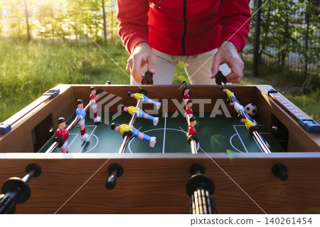 Man playing foosball outdoors in a garden, reflecting everyday recreation as a prelude to the upcoming global soccer championship Man playing foosball outdoors in a garden, reflecting everyday recreation as a prelude to the upcoming global soccer championship 140261454