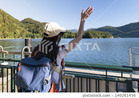 Woman waving on a pier at Lake Wolfgangsee in the Austrian Alps, illustrating summer lakeside travel and a nature tourism scene Woman waving on a pier at Lake Wolfgangsee in the Austrian Alps, illustrating summer lakeside travel and a nature tourism scene 140261456