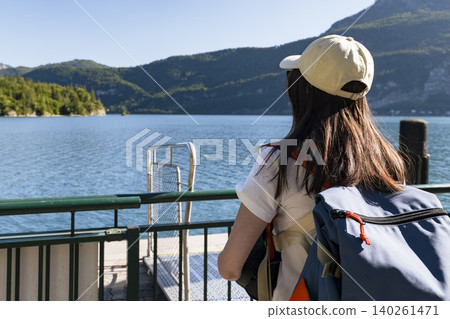 Young woman looking at the lake and mountains from a pier at Wolfgangsee in the Austrian Alps, expressing a connection with nature Young woman looking at the lake and mountains from a pier at Wolfgangsee in the Austrian Alps, expressing a connection with nature 140261471