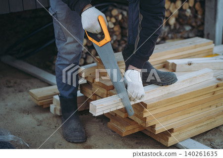An unrecognizable man cuts a wooden block with a hand saw during woodworking or construction work An unrecognizable man cuts a wooden block with a hand saw during woodworking or construction work 140261635