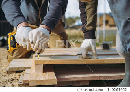 Close-up of a man hands driving a screw with a cordless drill while constructing a tall raised garden bed on a countryside property Close-up of a man hands driving a screw with a cordless drill while constructing a tall raised garden bed on a countryside property 140261652