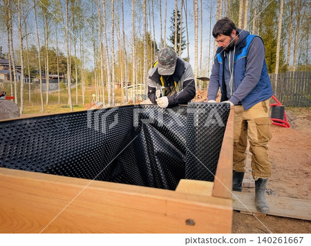 Handy men construct a tall raised garden bed from larch wood and line the inside with a protective membrane on countryside property Handy men construct a tall raised garden bed from larch wood and line the inside with a protective membrane on countryside property 140261667