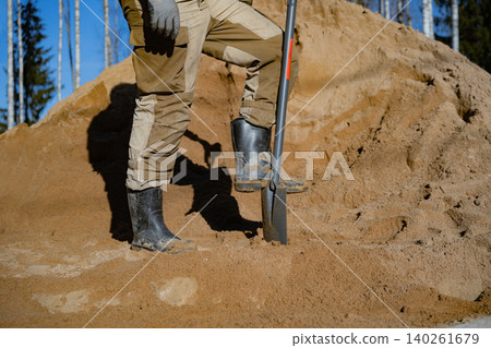 unrecognizable man stands with one foot on a shovel on his countryside property, posing during outdoor yard work. unrecognizable man stands with one foot on a shovel on his countryside property, posing during outdoor yard work. 140261679