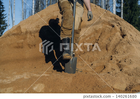 unrecognizable man stands with one foot on a shovel on his countryside property, posing during outdoor yard work. unrecognizable man stands with one foot on a shovel on his countryside property, posing during outdoor yard work. 140261680