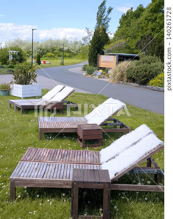 Wooden sun loungers with white fur throws on a green lawn Wooden sun loungers with white fur throws on a green lawn 140261728