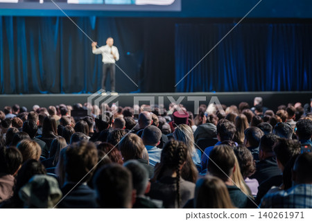 Large audience listening to speaker on stage at business conference with dim blue lighting Large audience listening to speaker on stage at business conference with dim blue lighting 140261971