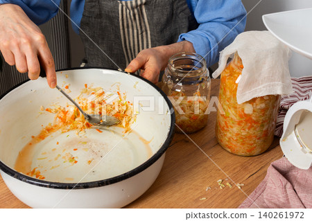 In a kitchen, a 53-year-old man works on fermenting cabbage and carrots. He carefully transfers the mixture into a glass jar for storage and fermentation In a kitchen, a 53-year-old man works on fermenting cabbage and carrots. He carefully transfers the mixture into a glass jar for storage and fermentation 140261972