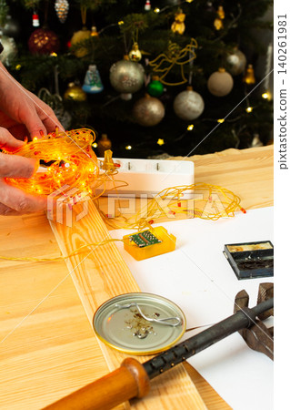 A man fixes a Christmas tree garland and lights on a table at home. He is checking the connection and making adjustments to ensure everything works for the holiday season 140261981